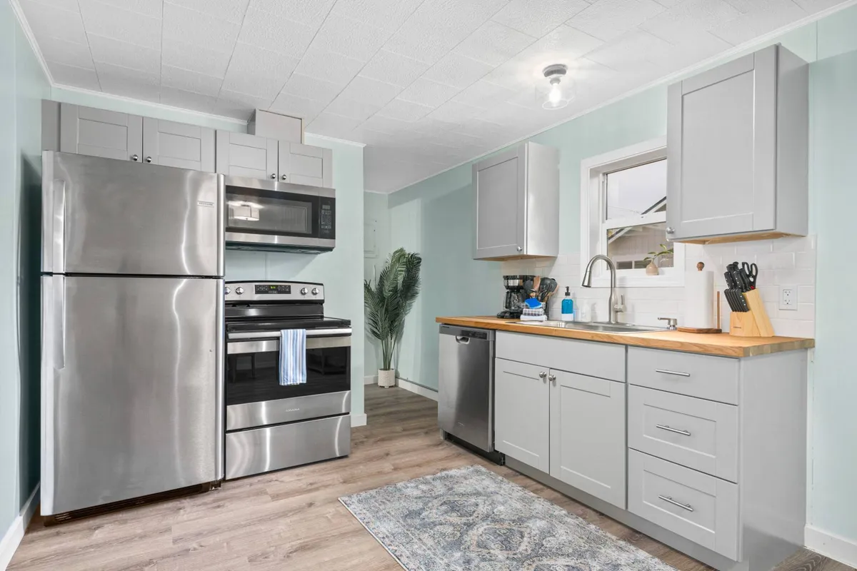 A crisp, modern kitchen with stainless steel appliances, wooden countertops, blue accents, and a window that brings in natural light. The kitchen is ready for meal prep or casual conversation, with a warm and stylish vibe that fits the updated, fully equipped kitchen described in the section.