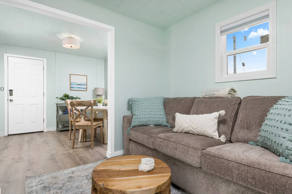 The image showcases a warm, inviting living space featuring a cozy sofa, a rustic wooden coffee table perfect for gatherings, a dining table ready for intimate meals, and tasteful artwork on the wall—all set in a light-filled interior that feels both relaxing and stylish.