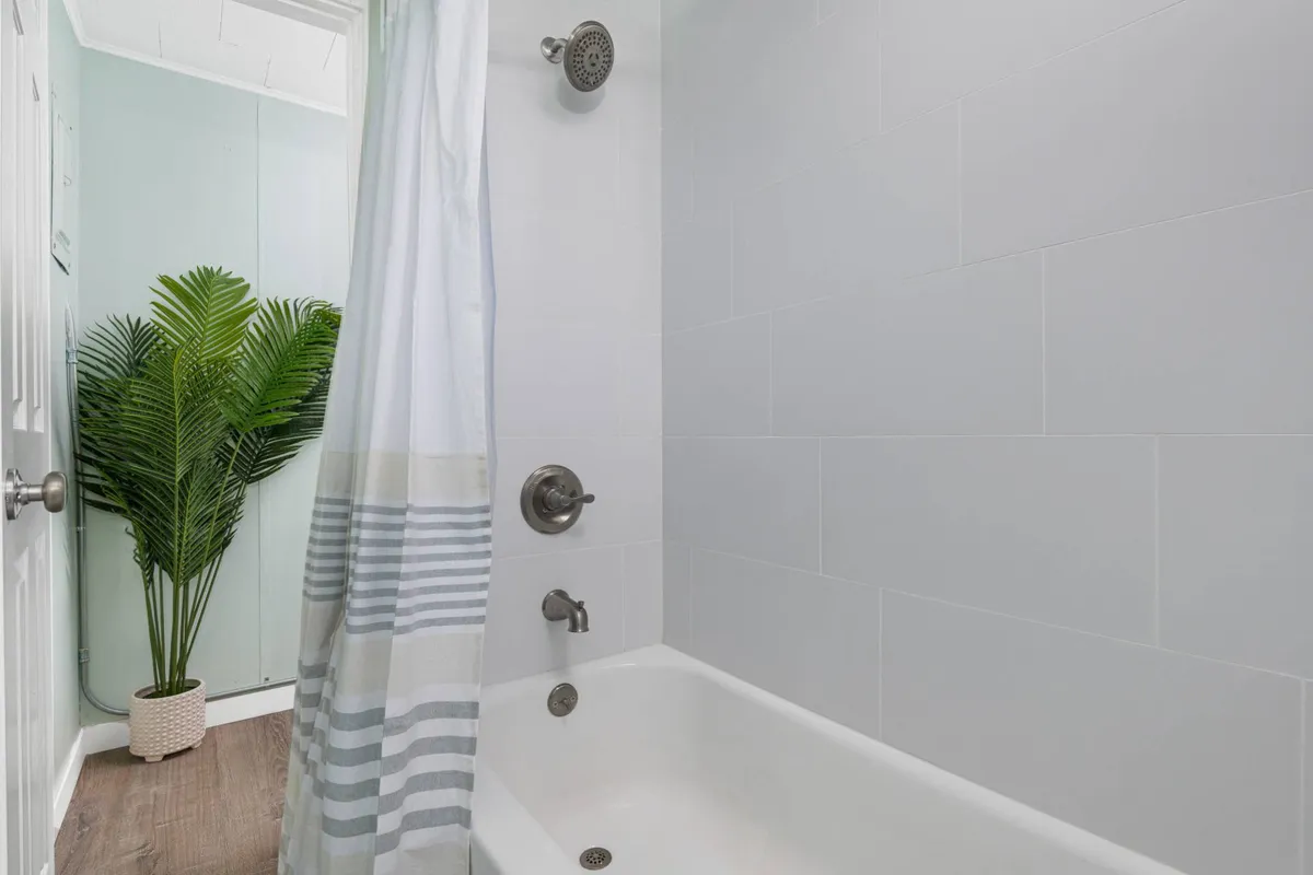 A bright, serene bathroom space featuring a clean white bathtub and shower, accented with a striped curtain and a small green plant. The scene evokes a sense of relaxation and calm, ideal for unwinding after a long day.