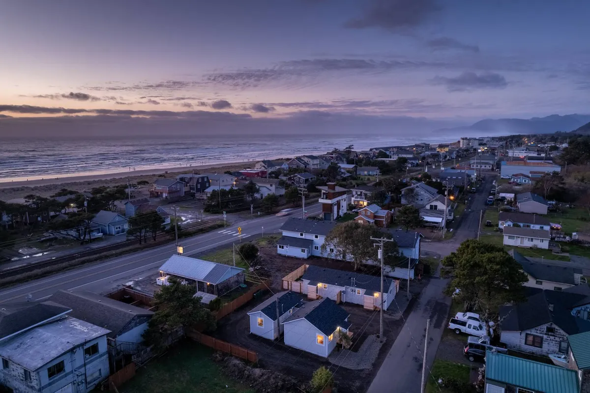 This image captures a sweeping ocean view framed by nearby houses and a quiet road, with the soft glow of streetlights suggesting evening. The scene conveys a serene setting ideal for sunset walks or relaxing beach activities just steps from home.